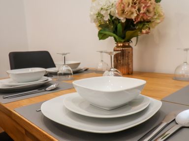 A dining table set with white plates bowls silverware and upside down wine glasses with flowers in a vase at The Bungalow in Whitby
