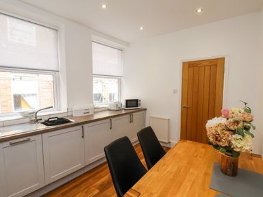 A kitchen with white cabinets wooden countertops a dining table with flowers in a vase and black chairs at The Bungalow in Whitby