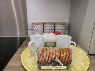 A kitchen counter with two white mugs biscuits in a package and three labeled canisters for tea coffee and sugar at The Bungalow in Whitby