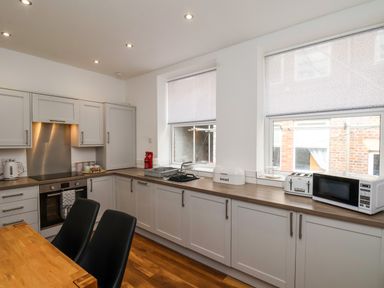 A kitchen with white cabinets black chairs a microwave toaster bread box and windows at The Bungalow in Whitby