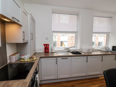 A kitchen with white cabinets wooden countertop and two windows with patterned blinds at The Bungalow in Whitby