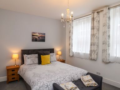 A bedroom with a double bed two bedside tables lamps a chandelier two windows and a bench at The Bungalow in Whitby