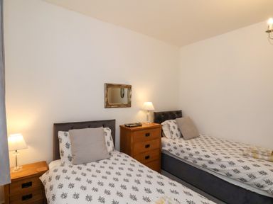 A bedroom with two single beds bedside tables lamps a chest of drawers and a wall mirror at The Bungalow in Whitby