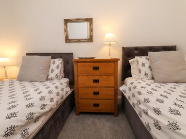 A bedroom with two single beds separated by a wooden dresser and lamps at The Bungalow in Whitby