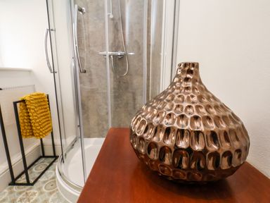 A bathroom with a curved glass shower enclosure a metallic vase on a wooden surface and yellow towels on a black towel rack at The Bungalow in Whitby