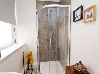 A bathroom with a corner shower enclosure a yellow towel on a rack artwork on the wall and a decorative vase on a wooden cabinet at The Bungalow in Whitby
