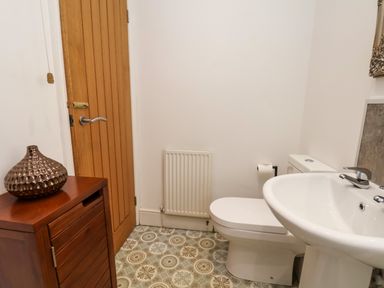 A bathroom with a sink toilet wooden cabinet with a decorative vase wooden door and patterned floor tiles at The Bungalow in Whitby