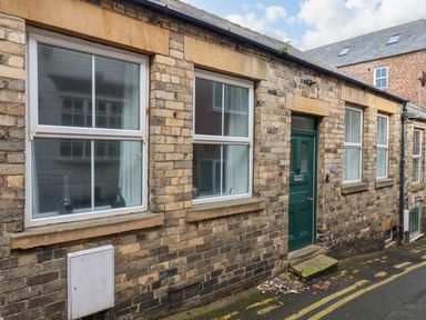 A row of brick houses with white framed windows and a green door on a narrow street at The Bungalow in Whitby