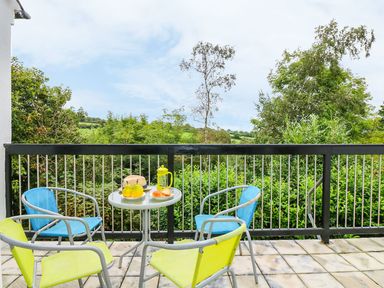 An outdoor balcony with a small round table and four chairs overlooking green trees at Tamar Cottages 35 in St Ann's Chapel Cornwall