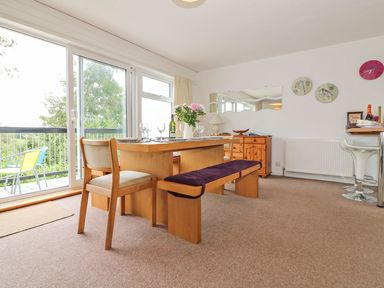 A dining room with a wooden table, chairs, bench, and sliding glass doors opening to a balcony at Tamar Cottages 35 in St Ann's Chapel Cornwall