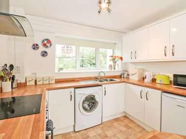 A kitchen with white cabinets a washing machine and a window above the sink at Tamar Cottages 35 in St Ann's Chapel Cornwall