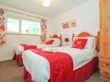 A bedroom with two single beds with red runners and pillows a wooden wardrobe and floral curtains at Tamar Cottages 35 in St Ann's Chapel Cornwall