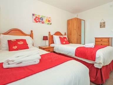 A bedroom with two single beds red cushions and throws wooden furniture and a floral painting on the wall at Tamar Cottages 35 in St Ann's Chapel Cornwall