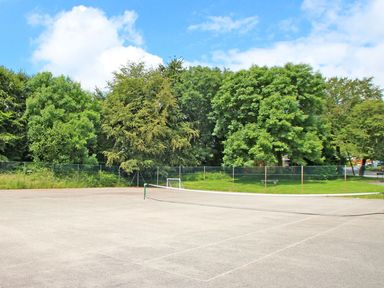 An outdoor tennis court with a net surrounded by trees and a grassy area at Tamar Cottages 35 in St Ann's Chapel Cornwall
