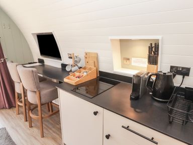 A kitchen counter with a kettle coffee machine knife block and stools next to a wall mounted TV at The Rowan Pod in Cowbridge
