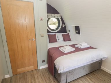 A bedroom with a double bed pillows and towels on the bed a round window and a wooden door at The Rowan Pod in Cowbridge