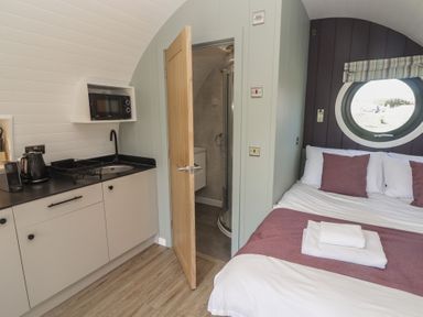 A small room with a kitchenette and bed next to a bathroom with an open door at The Rowan Pod in Cowbridge