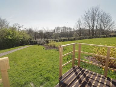 A grassy garden with a gravel path wooden railings and leafless trees at The Rowan Pod in Cowbridge
