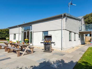 An outdoor patio with picnic tables, food, drinks, and a barbecue grill beside a modern house at Moult Hill Barn in Salcombe