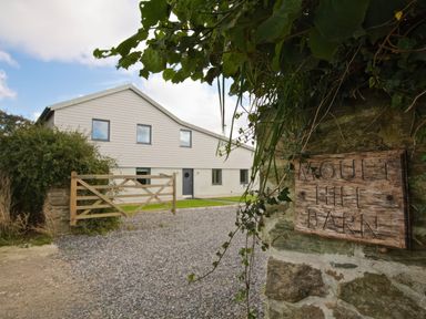 A modern barn-style building with gravel driveway and wooden gate at Moult Hill Barn in Salcombe