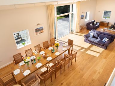 A dining area with a long wooden table set for a meal and a living area with two blue sofas at Moult Hill Barn in Salcombe