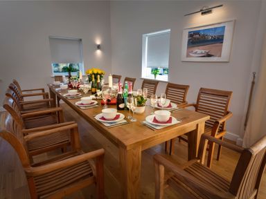 A dining room with a long wooden table set with bowls, wine glasses, bottles, candles, and wooden chairs at Moult Hill Barn in Salcombe