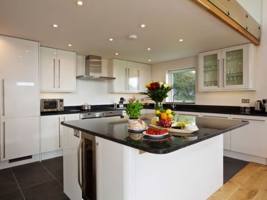 A kitchen with white cabinets a black countertop an island with food and flowers and a window showing trees at Moult Hill Barn in Salcombe