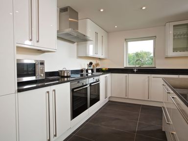 A kitchen with white cabinets black countertops a window and stainless steel appliances at Moult Hill Barn in Salcombe