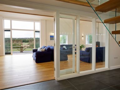 A living room with blue sofas and large windows overlooking a garden at Moult Hill Barn in Salcombe