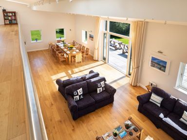 An open living and dining area with wooden floor large dining table sofas and glass doors leading outside at Moult Hill Barn in Salcombe