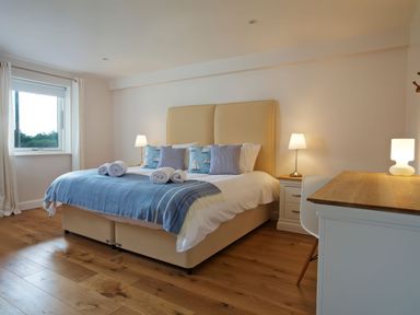 A bedroom with a double bed, bedside tables with lamps, a desk with a lamp, and a window at Moult Hill Barn in Salcombe