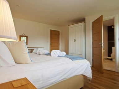 A bedroom with a bed with pillows and rolled towels a wardrobe two wooden doors and a lamp at Moult Hill Barn in Salcombe