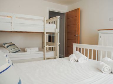 A bedroom with a bunk bed a white bed with rolled towels and a wooden door at Moult Hill Barn in Salcombe