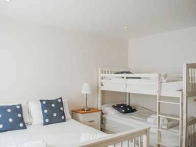 A bedroom with a double bed with blue polka dot pillows next to a wooden nightstand with a lamp and white bunk beds at Moult Hill Barn in Salcombe