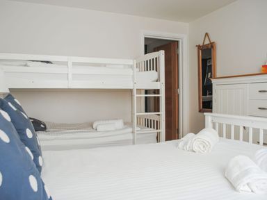 A bedroom with a bunk bed a large bed with towels a chest of drawers and a mirror at Moult Hill Barn in Salcombe