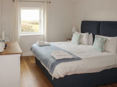 A bedroom with a double bed blue and white bedding and a window with curtains at Moult Hill Barn in Salcombe