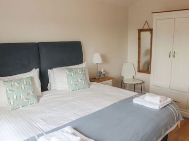 A bedroom with a bed with cushions and towels a chair a lamp a wardrobe and a mirror at Moult Hill Barn in Salcombe
