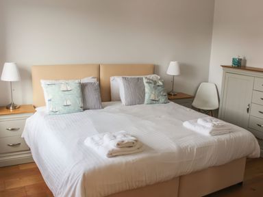 A bedroom with a bed with white linens pillows with sailboat designs bedside tables with lamps and a chair at Moult Hill Barn in Salcombe