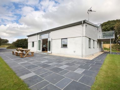 A modern house with a tiled patio and wooden picnic table in a rural setting at Moult Hill Barn in Salcombe