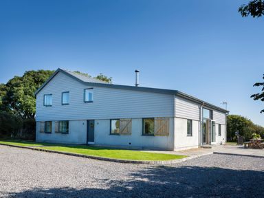 A modern two-story house with gray siding and wooden shutters surrounded by gravel and grass at Moult Hill Barn in Salcombe