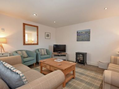 A living room with sofas armchairs a wooden coffee table a television and a small stove at Croft Cottage in Alnwick