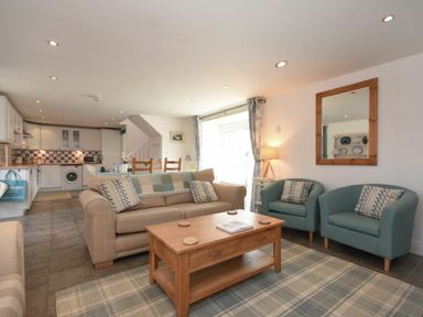 An open plan living room and kitchen with sofas, armchairs, coffee table, dining table, and kitchen appliances at Croft Cottage in Alnwick