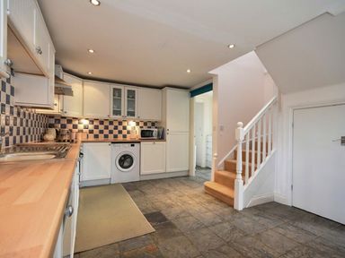 A kitchen with white cabinets a washing machine a microwave and stairs at Croft Cottage in Alnwick