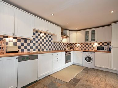 A kitchen with white cabinets blue and white checkered tile backsplash and appliances at Croft Cottage in Alnwick