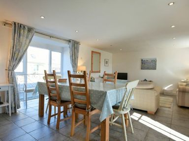 A dining area with a wooden table and chairs next to a window with curtains in an open living room at Croft Cottage in Alnwick
