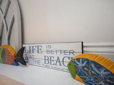 A shelf with a wooden sign that reads life is better at the beach and two colorful fish decorations at Croft Cottage in Alnwick