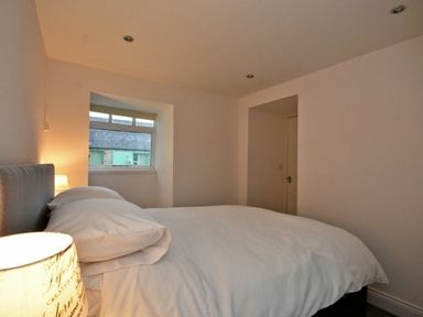 A bedroom with a bed a lamp a window and a door at Croft Cottage in Alnwick