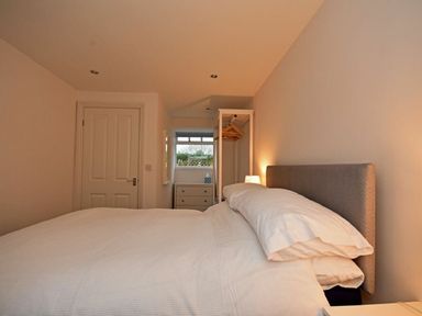 A bedroom with a bed white bedding a small dresser and a standing open wardrobe with hangers at Croft Cottage in Alnwick