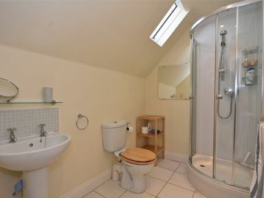 A bathroom with a sink toilet wooden shelving unit and corner shower at Croft Cottage in Alnwick