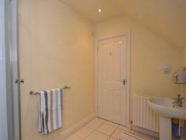 A bathroom with a towel rack holding a striped towel a door a radiator a sink with taps and a small mirror at Croft Cottage in Alnwick